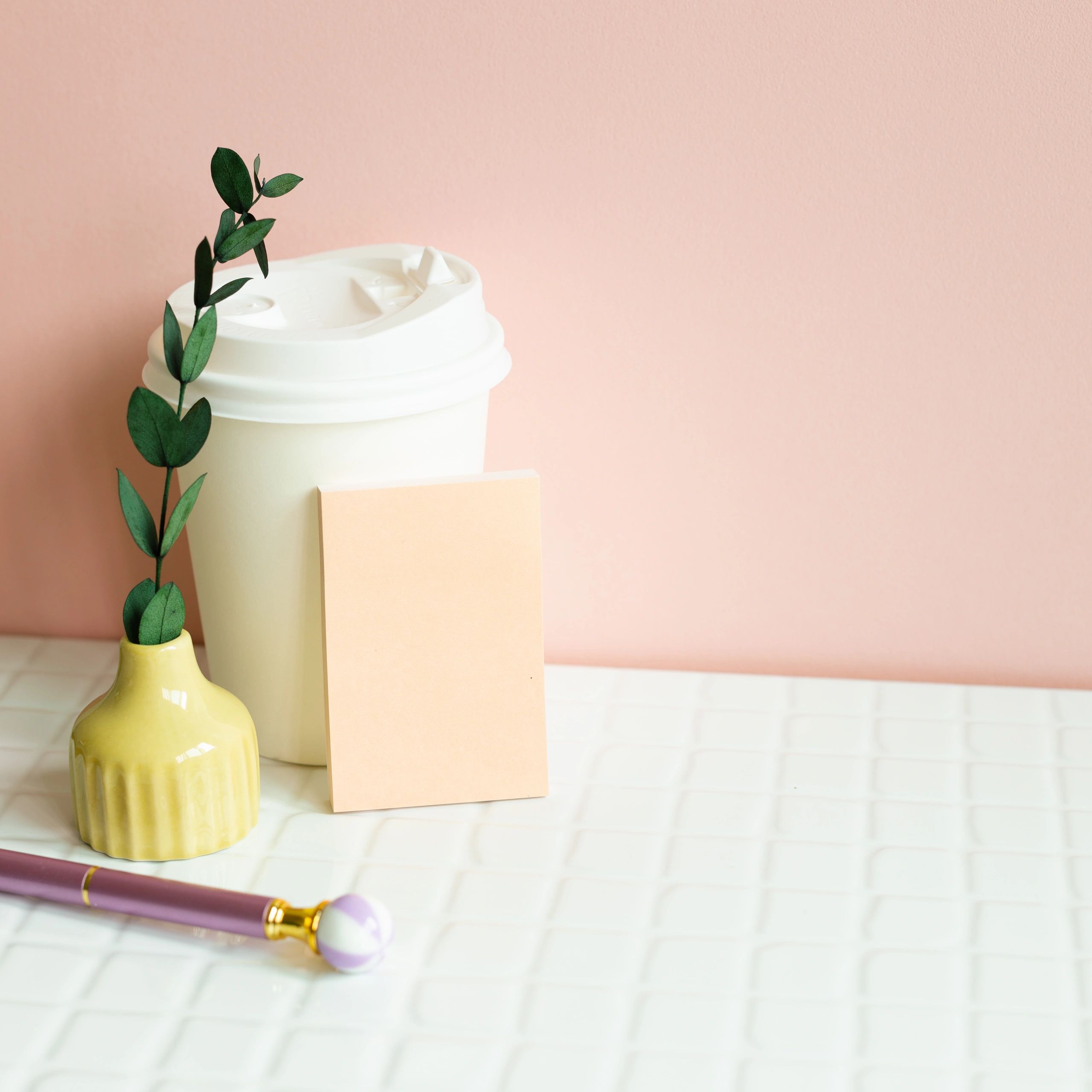 Styled pink desk workspace with coffee cup, memo pad, pen, and soft feminine decor