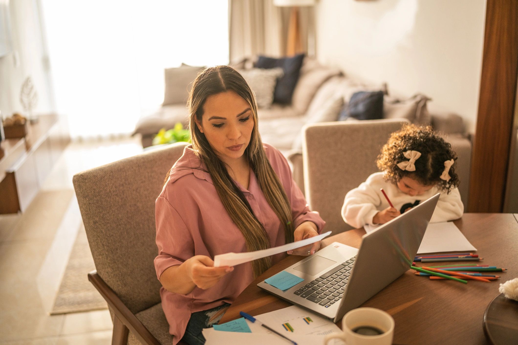 Young woman working while her daughter draws beside her at home
