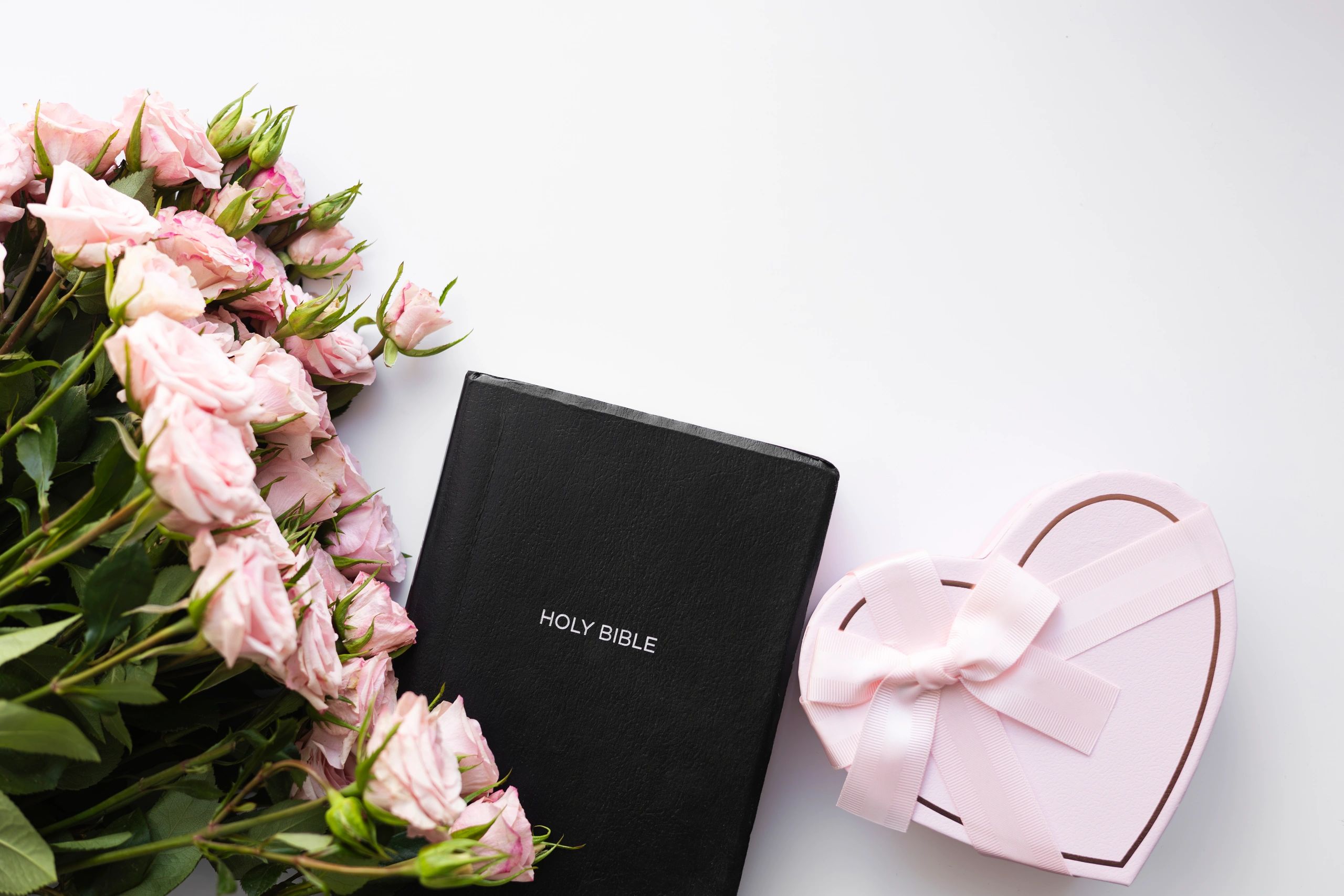 Bible with flowers and heart-shaped gift on white background